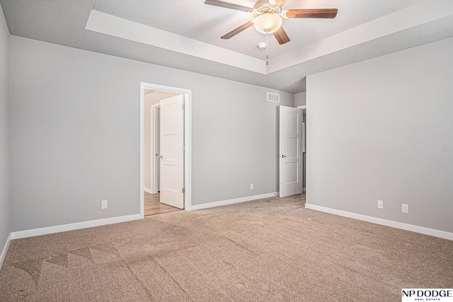 unfurnished bedroom featuring a tray ceiling, light colored carpet, and baseboards