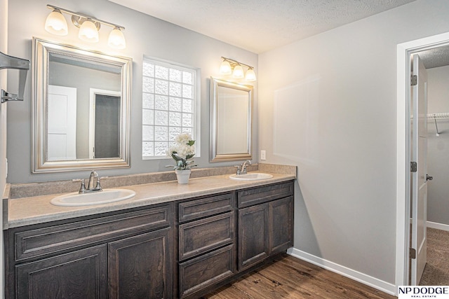 bathroom with a textured ceiling, baseboards, a sink, and wood finished floors