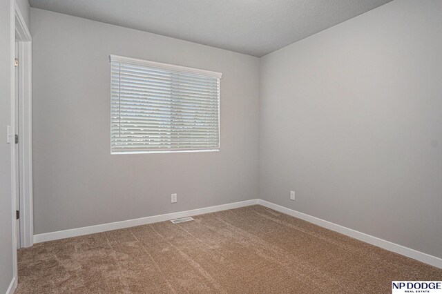 spare room with baseboards, a textured ceiling, visible vents, and light colored carpet