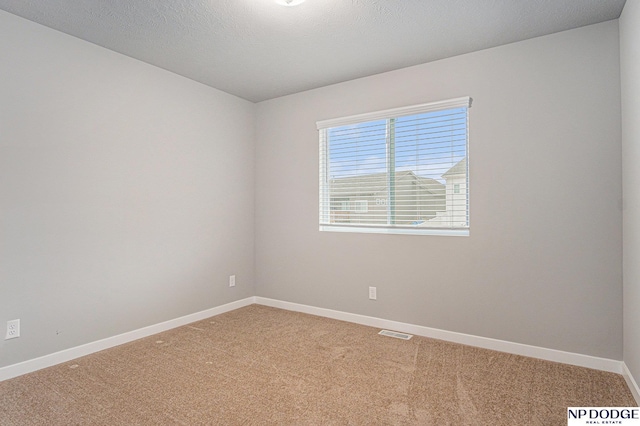 empty room featuring light colored carpet, visible vents, a textured ceiling, and baseboards