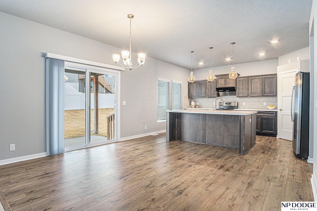 kitchen with tasteful backsplash, appliances with stainless steel finishes, wood finished floors, light countertops, and dark brown cabinets