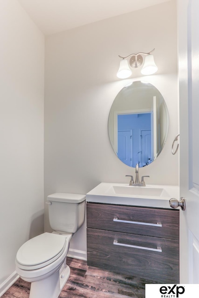 half bath with baseboards, vanity, toilet, and wood finished floors