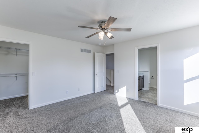 unfurnished bedroom with connected bathroom, visible vents, baseboards, carpet, and a walk in closet