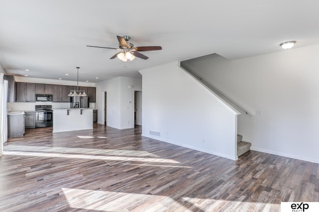 unfurnished living room featuring visible vents, stairway, a ceiling fan, wood finished floors, and baseboards