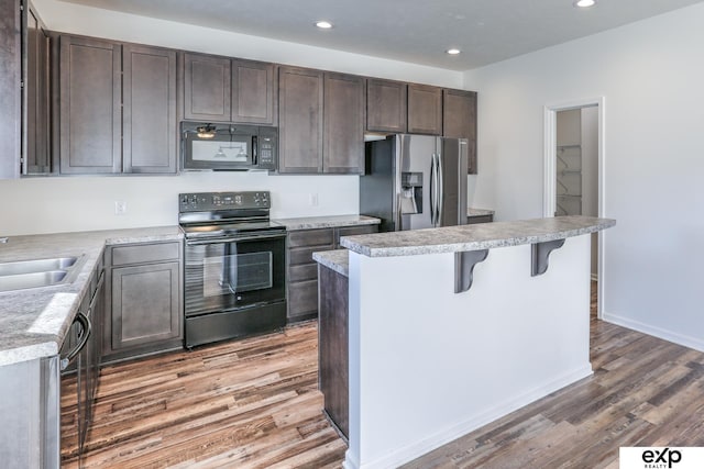 kitchen with light countertops, black appliances, dark brown cabinets, light wood-type flooring, and a kitchen bar