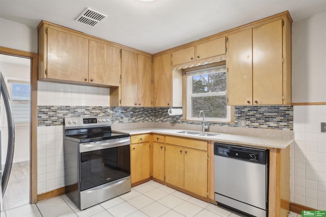 kitchen with visible vents, a sink, stainless steel appliances, light countertops, and tile walls