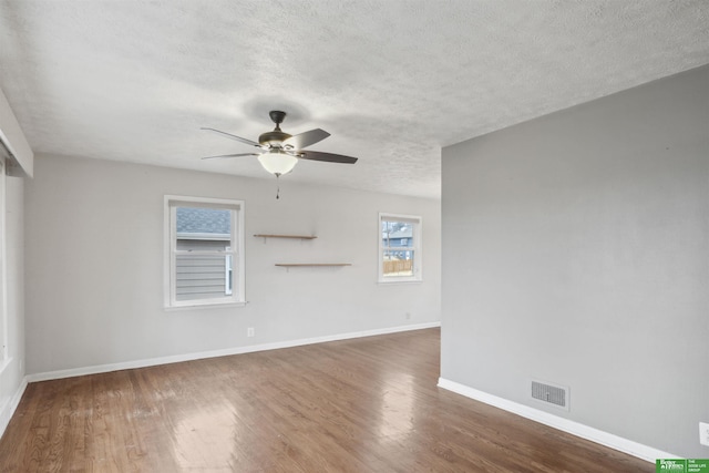 empty room with baseboards, visible vents, ceiling fan, wood finished floors, and a textured ceiling