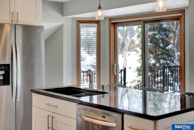 kitchen featuring white cabinets, dark countertops, appliances with stainless steel finishes, pendant lighting, and a sink