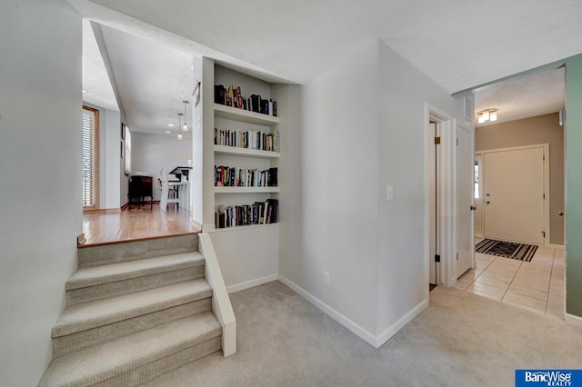 stairway featuring carpet, built in shelves, baseboards, and tile patterned flooring