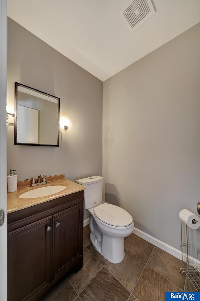 bathroom featuring toilet, vanity, visible vents, and baseboards