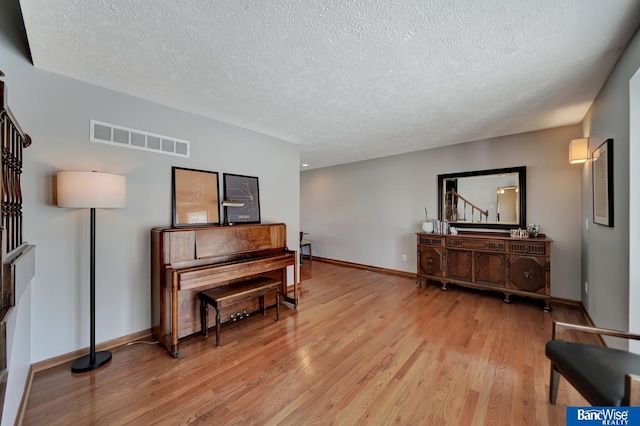 sitting room with light wood-style flooring, a textured ceiling, visible vents, and baseboards