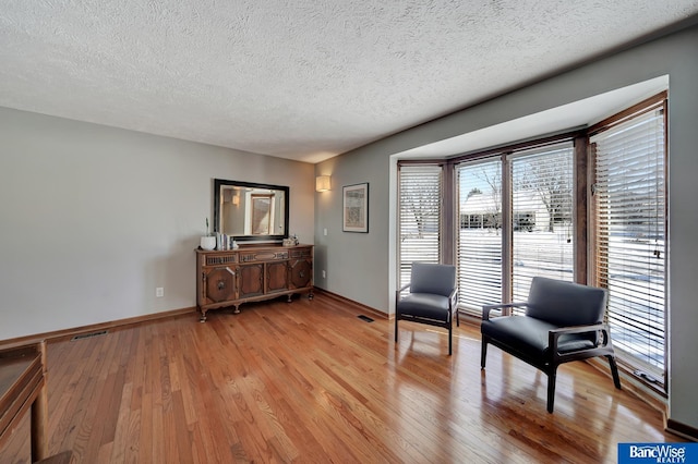 living area featuring light wood-type flooring, visible vents, a textured ceiling, and baseboards