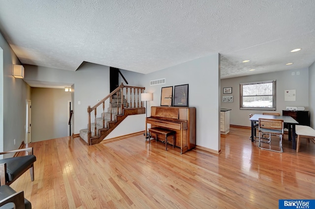 living area featuring baseboards, visible vents, stairway, wood finished floors, and a textured ceiling