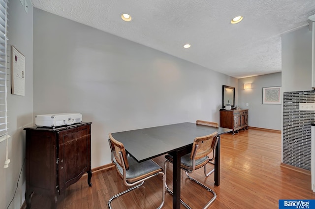 dining space with light wood-style flooring, a textured ceiling, and recessed lighting