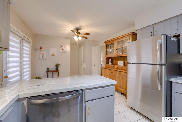 kitchen featuring light tile patterned floors, ceiling fan, light stone counters, appliances with stainless steel finishes, and glass insert cabinets