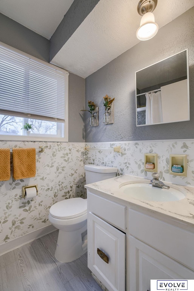 full bath with a textured wall, vanity, wood finished floors, and toilet