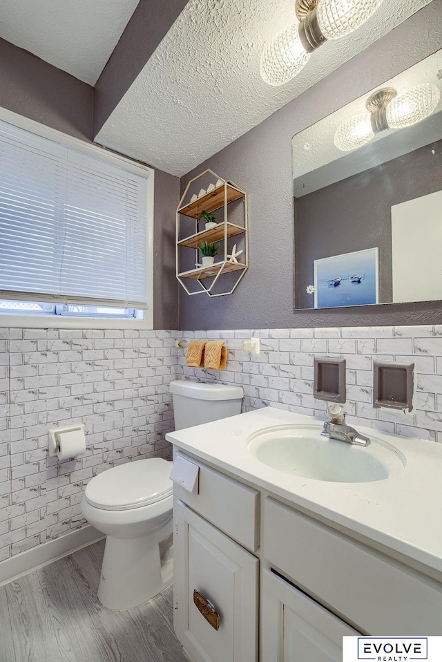 half bath featuring toilet, a wainscoted wall, wood finished floors, a textured ceiling, and vanity