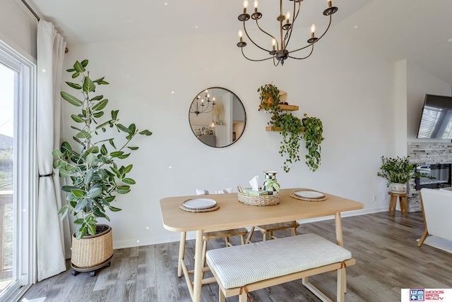 dining room featuring a notable chandelier, a fireplace, baseboards, and wood finished floors