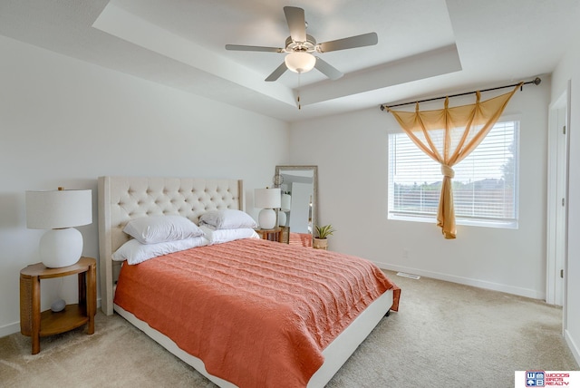 bedroom with a tray ceiling, light carpet, ceiling fan, and baseboards