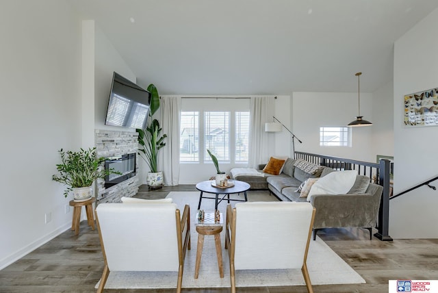 living area featuring a healthy amount of sunlight, baseboards, wood finished floors, and a stone fireplace