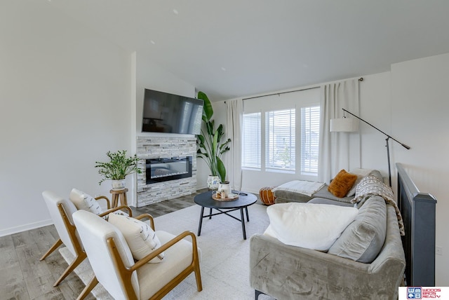 living room featuring lofted ceiling, a stone fireplace, wood finished floors, and baseboards