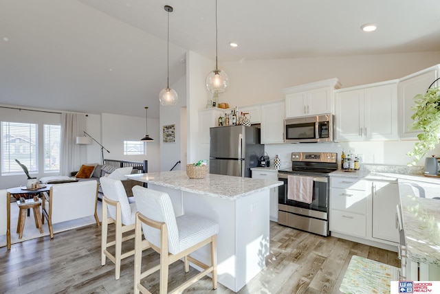 kitchen with light stone countertops, white cabinets, appliances with stainless steel finishes, a center island, and light wood finished floors