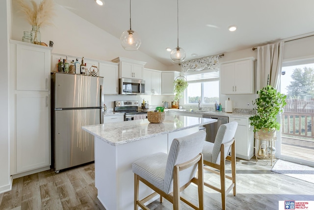 kitchen with lofted ceiling, light wood-style flooring, stainless steel appliances, a kitchen island, and white cabinets