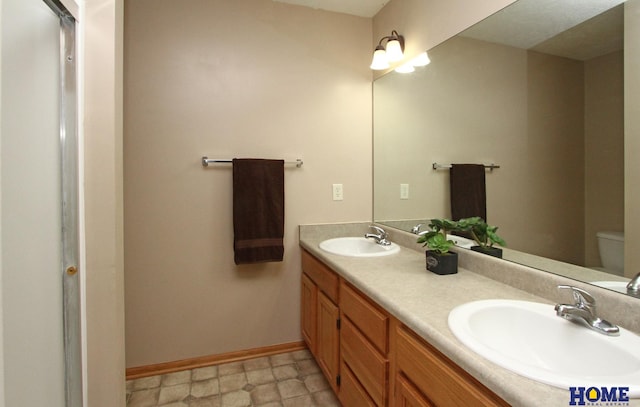 bathroom featuring double vanity, baseboards, toilet, and a sink