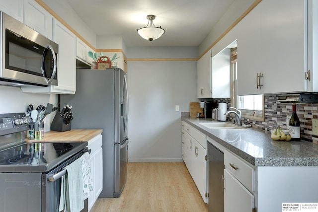 kitchen with stainless steel appliances, decorative backsplash, white cabinets, a sink, and light wood-type flooring