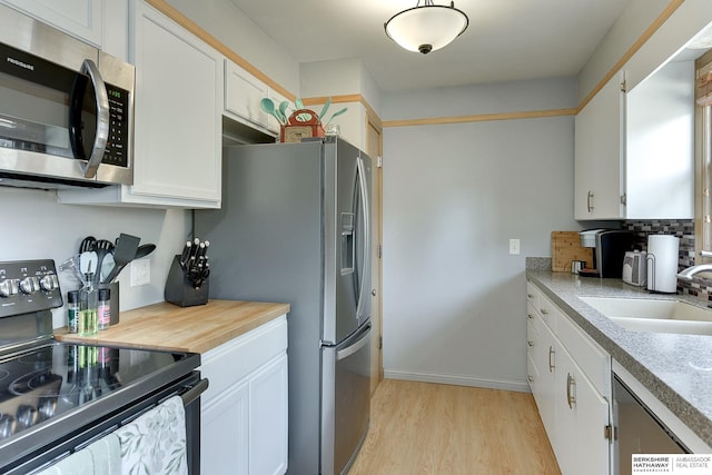 kitchen with light wood finished floors, decorative backsplash, appliances with stainless steel finishes, white cabinetry, and a sink