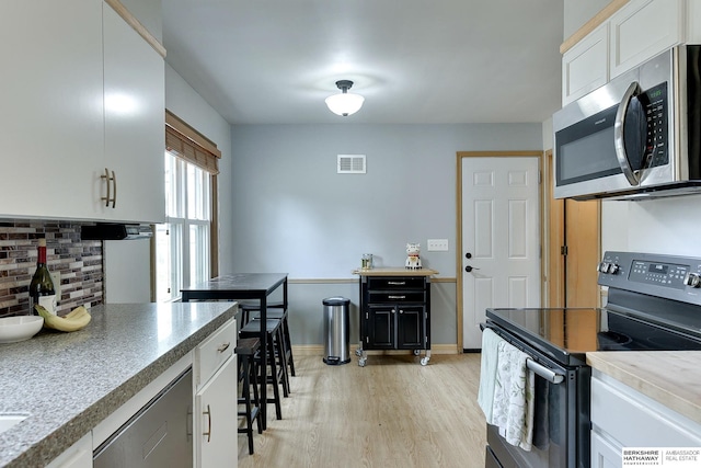 kitchen featuring visible vents, white cabinets, decorative backsplash, light wood-style flooring, and stainless steel appliances