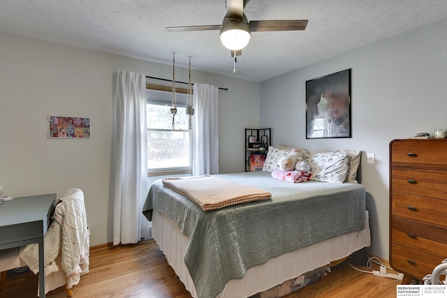 bedroom featuring a ceiling fan, a textured ceiling, baseboards, and wood finished floors