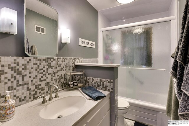 bathroom featuring toilet, shower / bath combination with glass door, visible vents, vanity, and tile walls