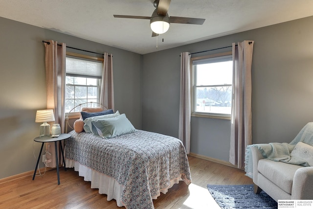 bedroom with a ceiling fan, light wood-type flooring, multiple windows, and baseboards