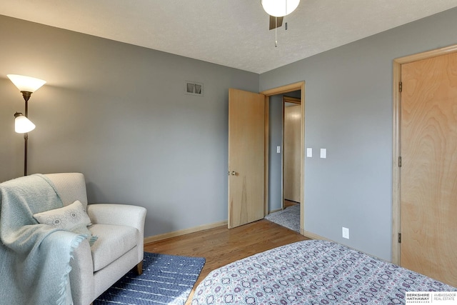 bedroom with visible vents, a textured ceiling, baseboards, and wood finished floors