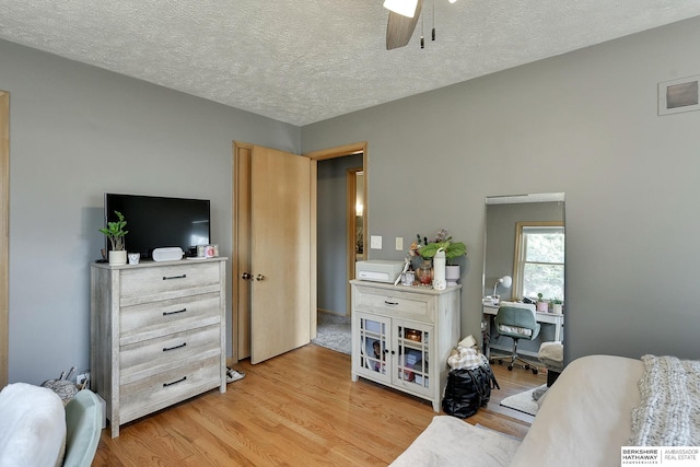 bedroom with light wood-style floors, visible vents, ceiling fan, and a textured ceiling