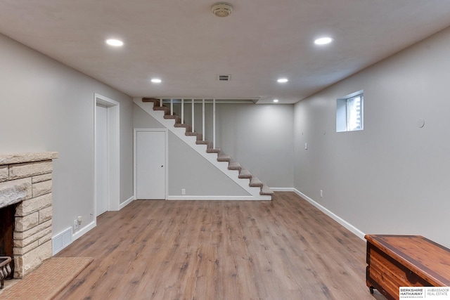 below grade area featuring visible vents, stairway, a stone fireplace, wood finished floors, and baseboards