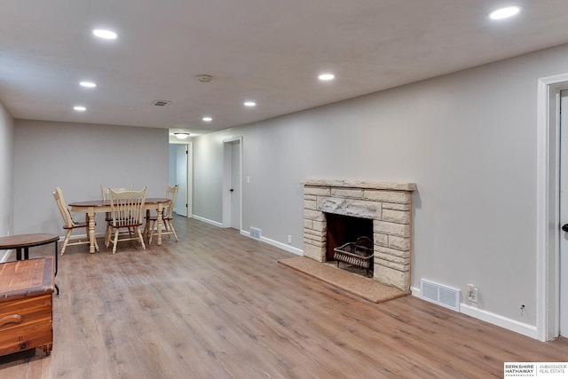 living room with a stone fireplace, wood finished floors, visible vents, and recessed lighting