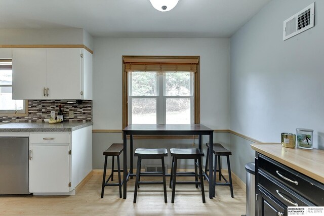 kitchen with light wood finished floors, visible vents, backsplash, white cabinets, and baseboards