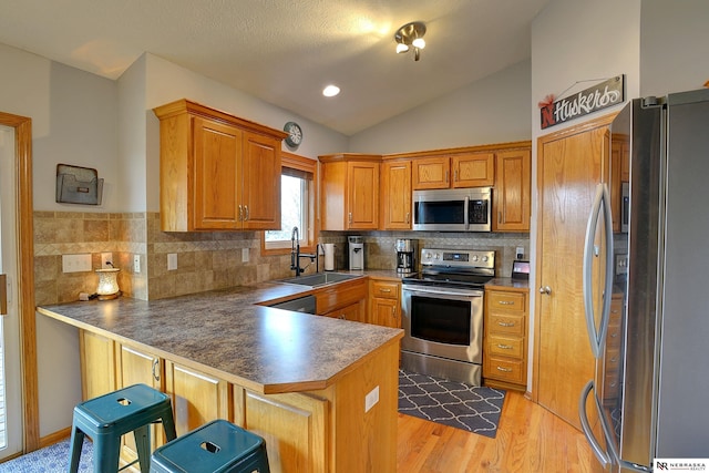 kitchen featuring stainless steel appliances, lofted ceiling, a sink, light wood-type flooring, and a peninsula