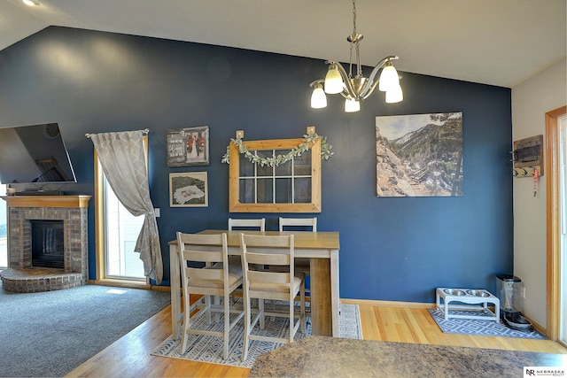 dining area with a fireplace, vaulted ceiling, wood finished floors, a chandelier, and baseboards