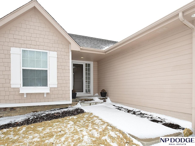 snow covered property entrance featuring a shingled roof