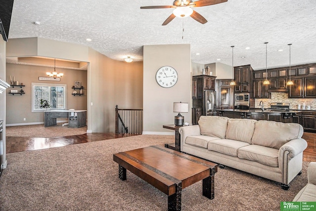 living area featuring ceiling fan with notable chandelier, a textured ceiling, baseboards, and wood finished floors