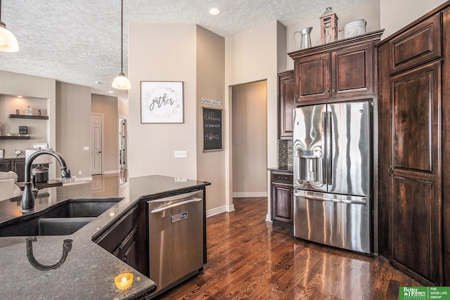 kitchen with dark stone counters, a sink, dark wood-type flooring, dark brown cabinetry, and appliances with stainless steel finishes