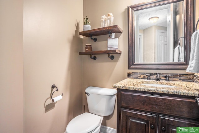 half bathroom with baseboards, toilet, vanity, decorative backsplash, and a textured ceiling