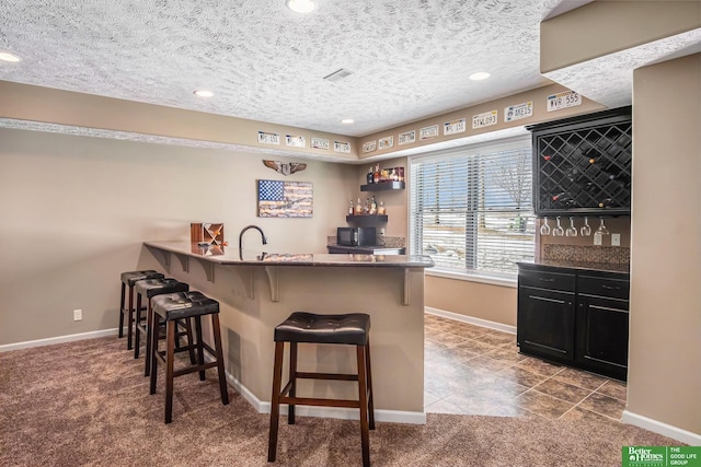 kitchen with carpet floors, a textured ceiling, a breakfast bar, and a peninsula