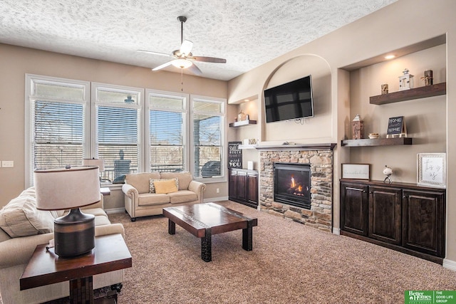 carpeted living area featuring baseboards, a textured ceiling, a stone fireplace, and a ceiling fan