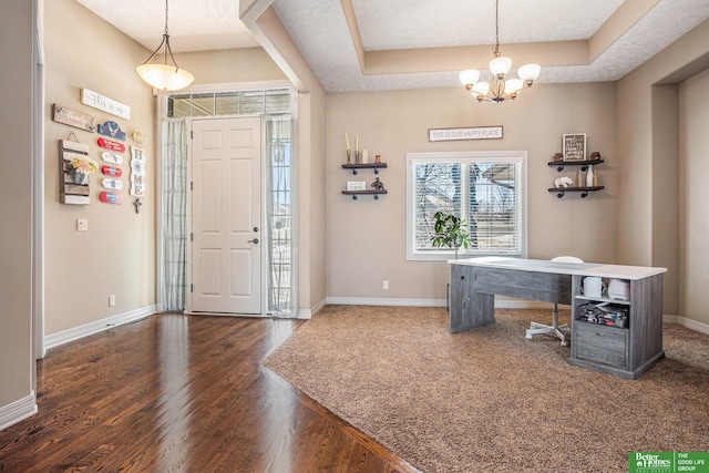 foyer with an inviting chandelier, a raised ceiling, baseboards, and wood finished floors