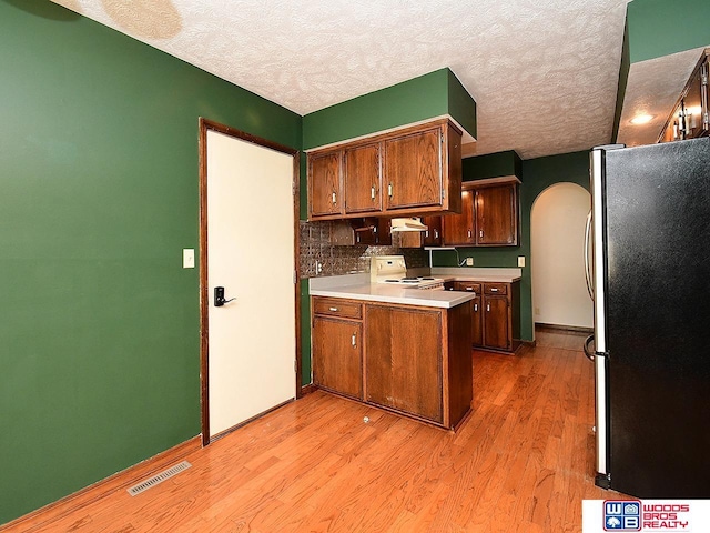 kitchen featuring arched walkways, electric stove, visible vents, freestanding refrigerator, and a peninsula