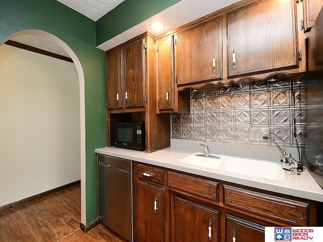 kitchen featuring arched walkways, light countertops, stainless steel dishwasher, a sink, and black microwave